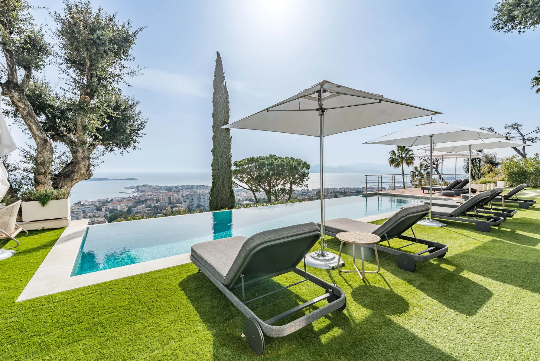 Piscine à débordement avec bains de soleil et parasols, vue baie de Cannes
