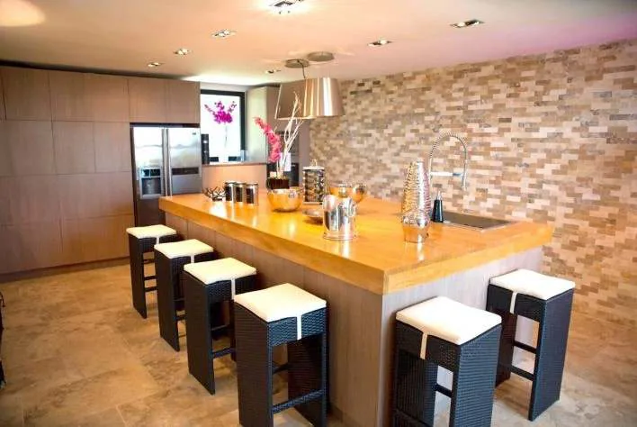 Cuisine americaine equipee avec ilot central en bois, hotte design et tabourets de bar