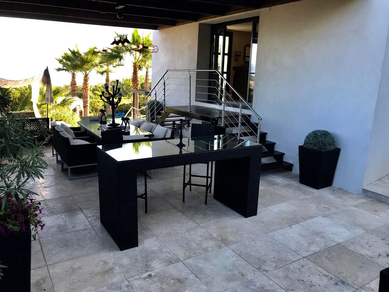Espace dining exterieur avec table bar en rotin noir, salon lounge et escalier vers la piscine