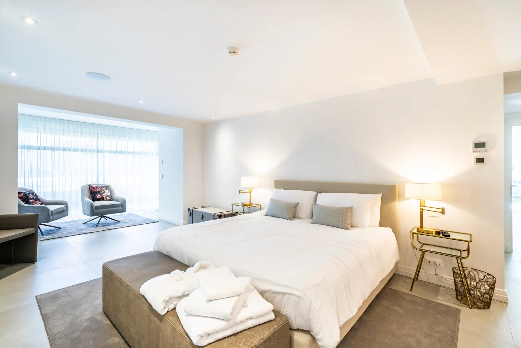 Chambre double avec lit beige, fauteuil et baies vitrées voilage