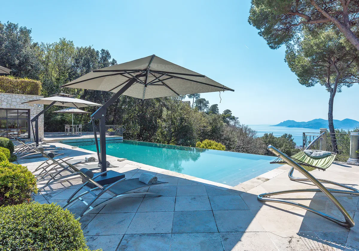 Piscine à débordement entourée de pins parasols vue mer
