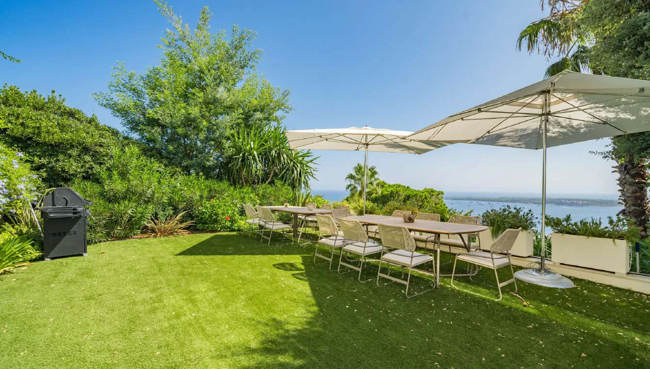 Salle à manger extérieure sur la pelouse avec barbecue et vue baie