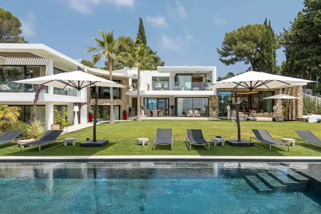Vue d'ensemble villa contemporaine, piscine et parasols, façade pierre et baies vitrées