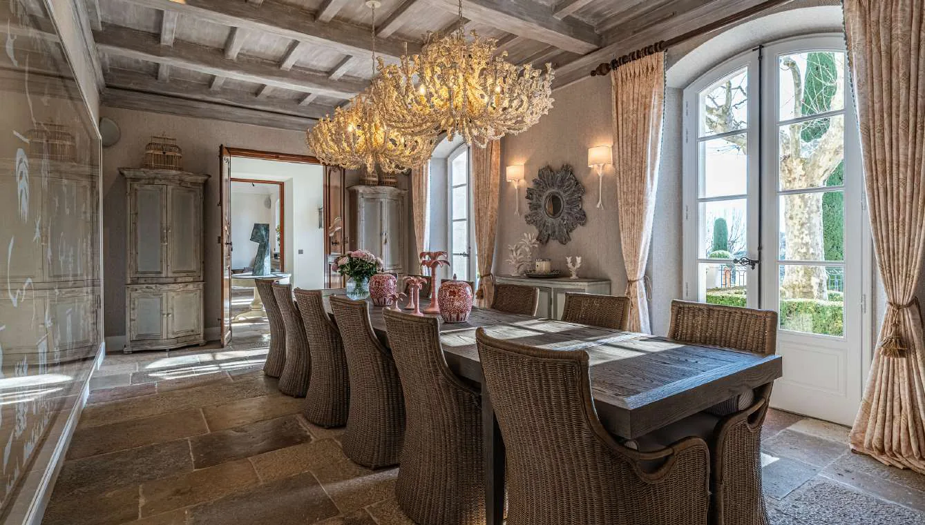 Salle a manger avec lustre dore, cheminee en pierre et baies vitrees jardin