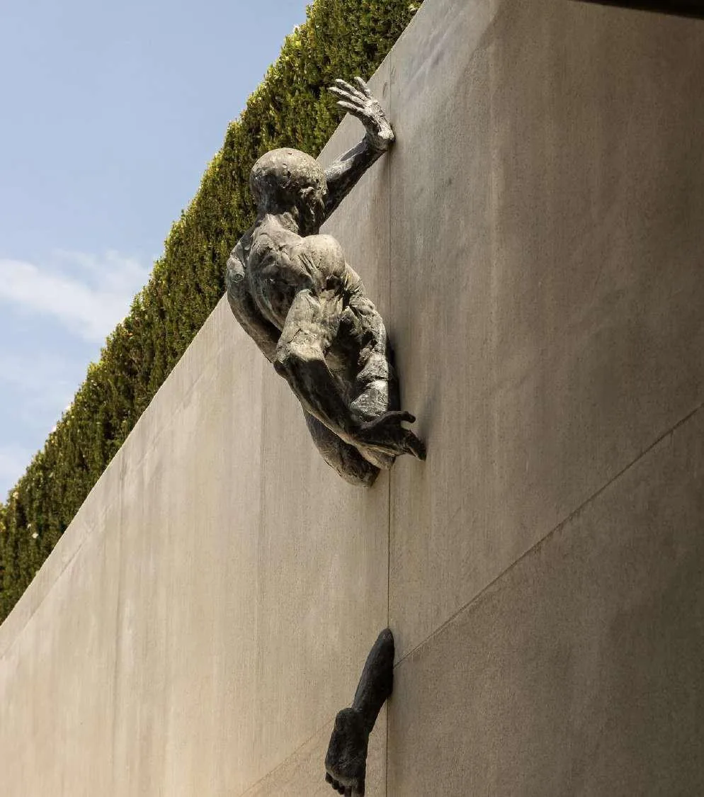 Détail d'une sculpture bronze de figure escaladant un mur en pierre dans le jardin