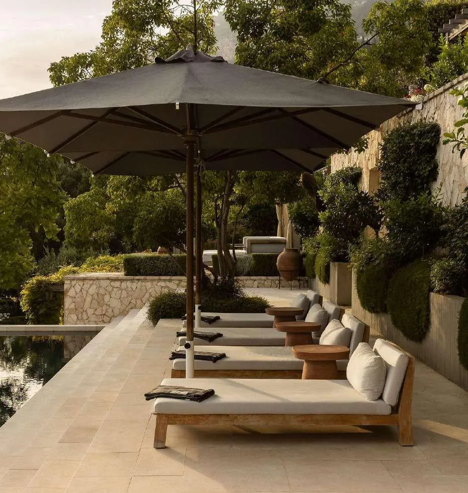 Vue latérale d'un parasol et bain de soleil avec haie taillée en arrière-plan